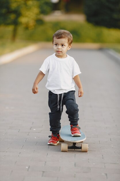 Child in a summer park. Boy in a white t-shirt. Kid with skate.