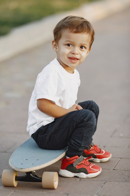 Ребенок в летнем парке. Мальчик в белой футболке. Малыш с коньком.