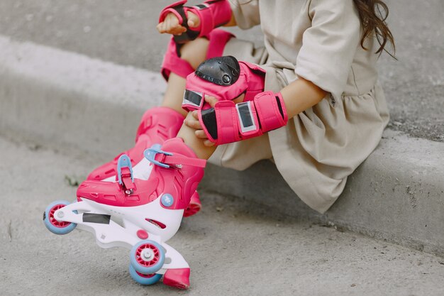 Child in a summer park. Kid in a pink helmet. Little girl with a roller.