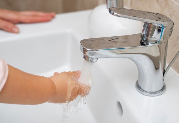 Ребенок моет руки дома с помощью мамы