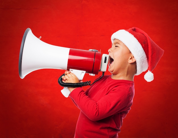 Free photo child wearing santa hat and shouting with a megaphone