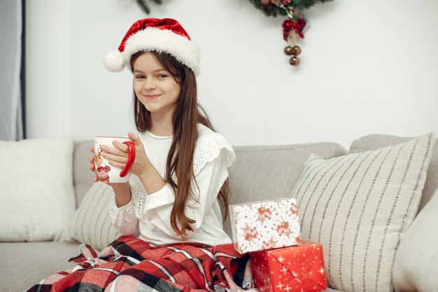 Child in a white sweater. Daughter sitting near Christmas tree.