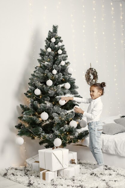 Child in a white sweater. Daughter standing near Christmas tree.