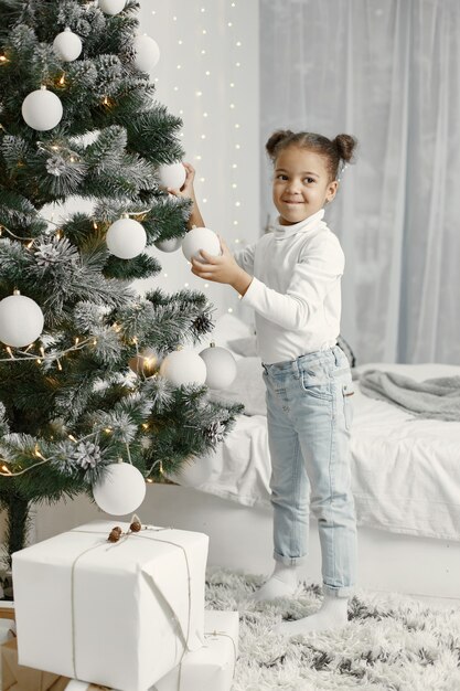 Child in a white sweater. Daughter standing near Christmas tree.