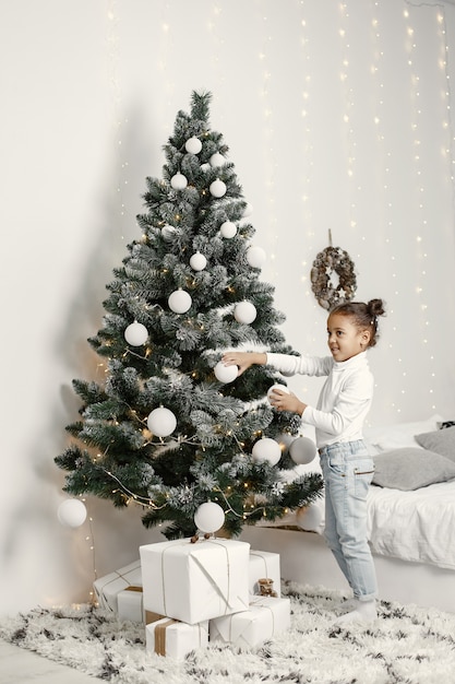 白いセーターを着た子供。クリスマスツリーの近くに立っている娘。