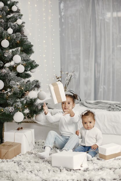 白いセーターを着た子供。クリスマスツリーの近くに座っている娘。家に2人の姉妹。