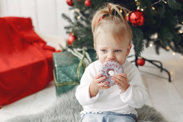 白いセーターを着た子供が遊んでいます。娘がクリスマスツリーの近くに立っています。