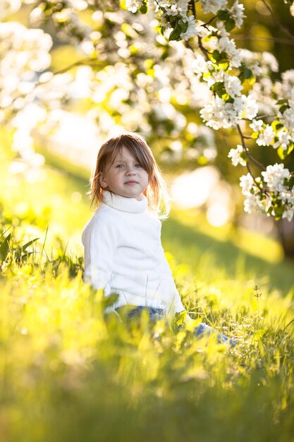 Child in white sweater and jeans spring flowers