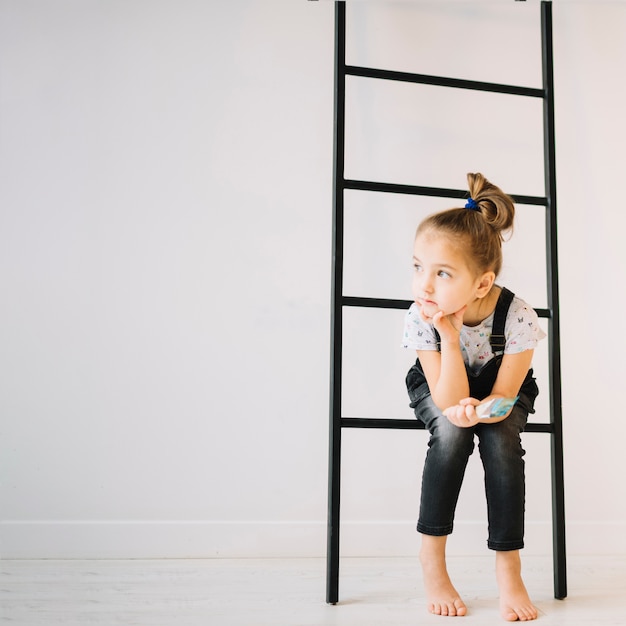 Child with brush sitting on ladder near wall in room