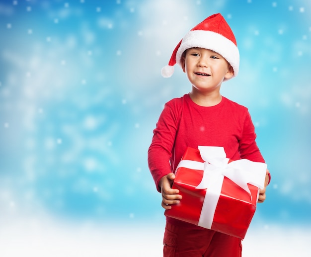 Bambino con un regalo rosso in uno sfondo innevato