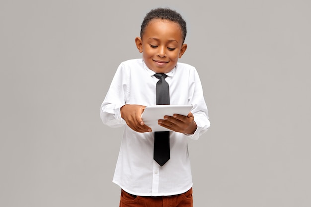 Childhood, modern technology and addiction. cute Afro American schoolboy addicted to electronic gadgets using digital tablet to play video games, having absorbed facial expression