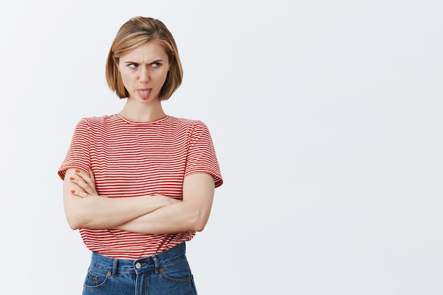 Infantile ragazza disgustata che mostra la lingua e guardando a destra infastidita, esprime avversione