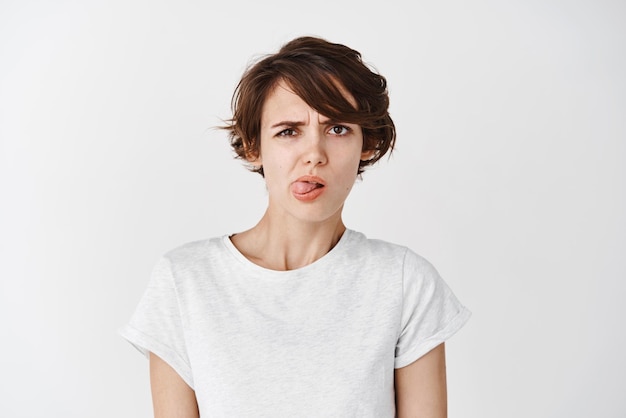 Childish woman showing tongue and grimacing from dislike or aversion disgusted with something white background