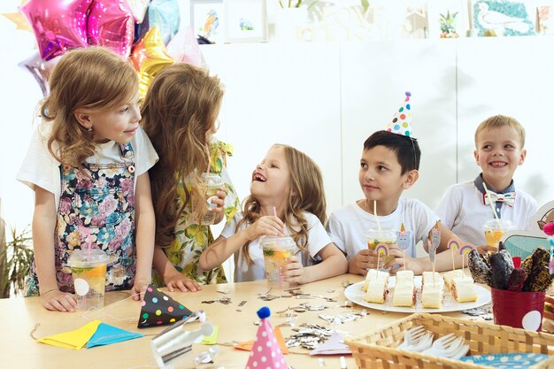 子供と誕生日の飾り。食べ物、ケーキ、飲み物、パーティーガジェットを備えたテーブルセッティングの男の子と女の子。