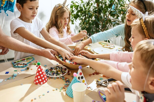 子供と誕生日の飾り。食べ物、ケーキ、飲み物、パーティーガジェットを備えたテーブルセッティングの男の子と女の子。