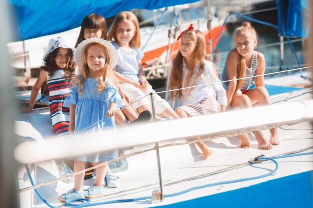 オレンジジュースを飲む海のヨットに乗っている子供たち。屋外の青い空に対して10代または子供の女の子。カラフルな服。キッズファッション、晴れた夏、川、休日のコンセプト。