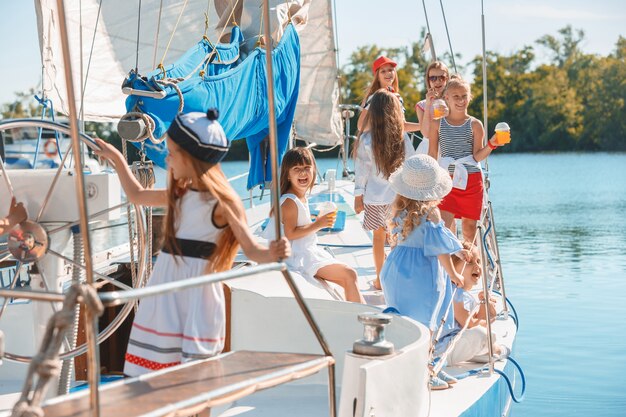 The children on board of sea yacht drinking orange juice. The teen or child girls against blue sky outdoor. 