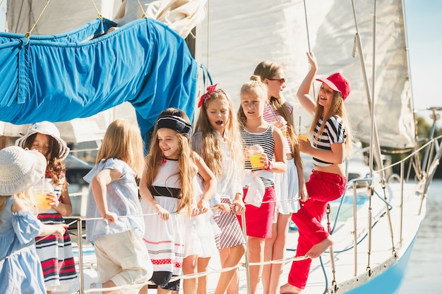 オレンジジュースを飲む海のヨットに乗っている子供たち。屋外の青い空に対して10代または子供の女の子