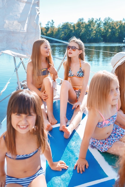 The children on board of sea yacht. The teen or child girls against blue sky outdoor. Colorful clothes. Kids fashion, sunny summer, river and holidays concepts.