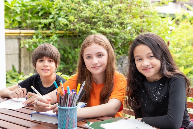 Children boy and girl doing homework and drawing together in garden at home looking at camera