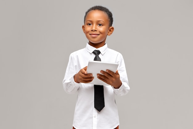 어린이, 전자 기기 및 가제트 개념. 그의 손에 휴대용 터치 패드 컴퓨터, 인터넷 서핑 또는 온라인 쇼핑으로 고립 된 유니폼 포즈의 스마트 자신감 아프리카 학생