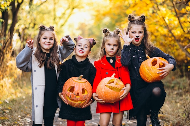 Children girls dressed in halloween costumes outdoors with pumpkins