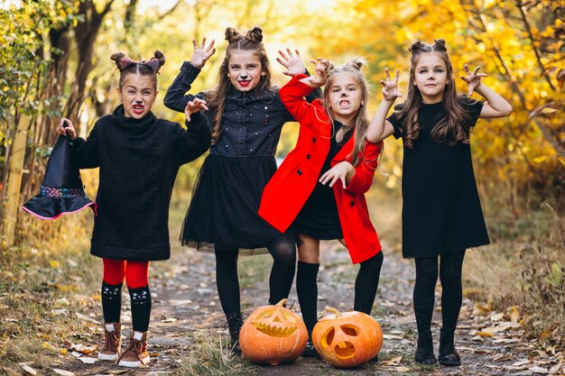 Children girls dressed in halloween costumes outdoors with pumpkins