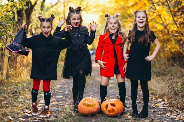 Children girls dressed in halloween costumes outdoors with pumpkins