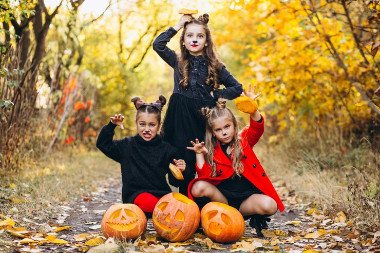 Free Photo children girls dressed in halloween costumes outdoors with pumpkins