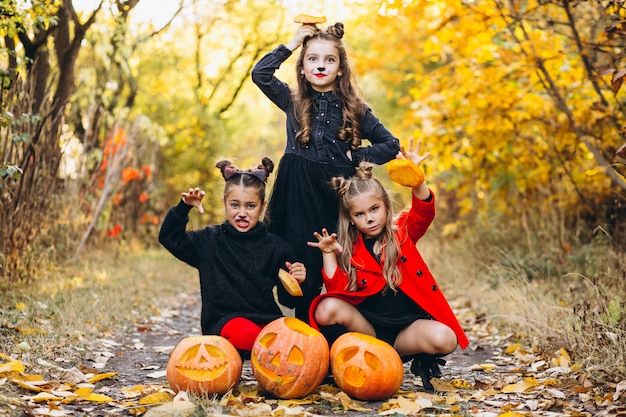 Children girls dressed in halloween costumes outdoors with pumpkins