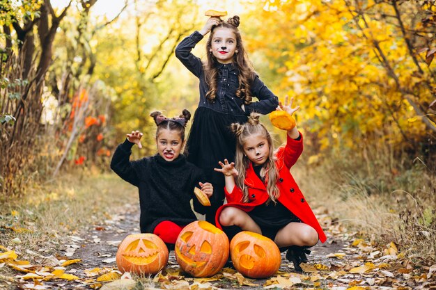 Children girls dressed in halloween costumes outdoors with pumpkins