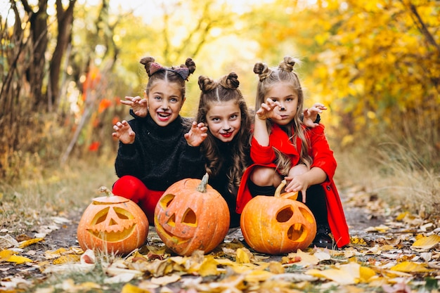 Children girls dressed in halloween costumes outdoors with pumpkins