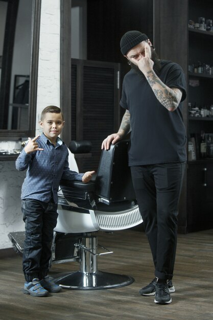 子供の美容師が暗い背景に小さな男の子をカットします。