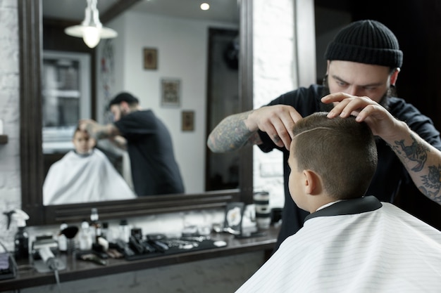 Children hairdresser cutting little boy against a dark background.