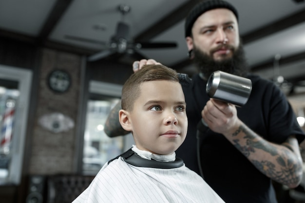 Детский парикмахер резки маленького мальчика на темном фоне.