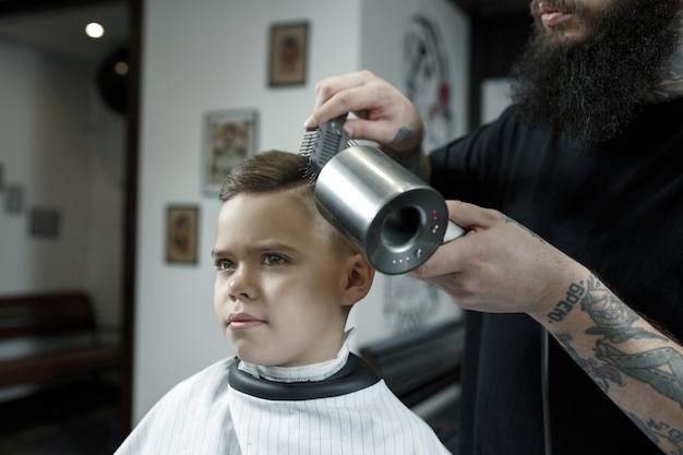 Детский парикмахер резки маленького мальчика на темном фоне.