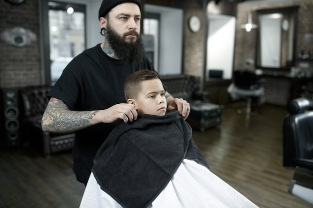 Children hairdresser cutting little boy against a dark background.