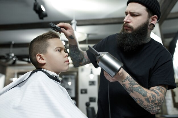 Children hairdresser cutting little boy against a dark