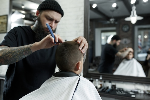 Children hairdresser cutting little boy against a dark