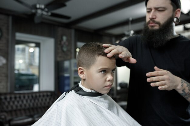 Children hairdresser cutting little boy against a dark