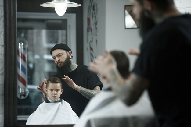 Children hairdresser cutting little boy against a dark