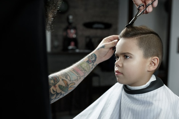 Children hairdresser cutting little boy in a barbershop