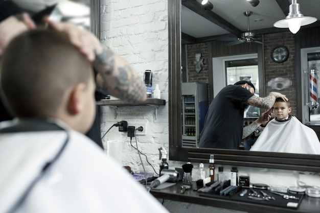 Children hairdresser cutting little boy in a barbershop