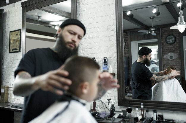 Children hairdresser cutting little boy in a barbershop