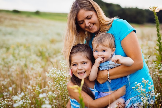 Children hug their mom standing on the field with white flowers 