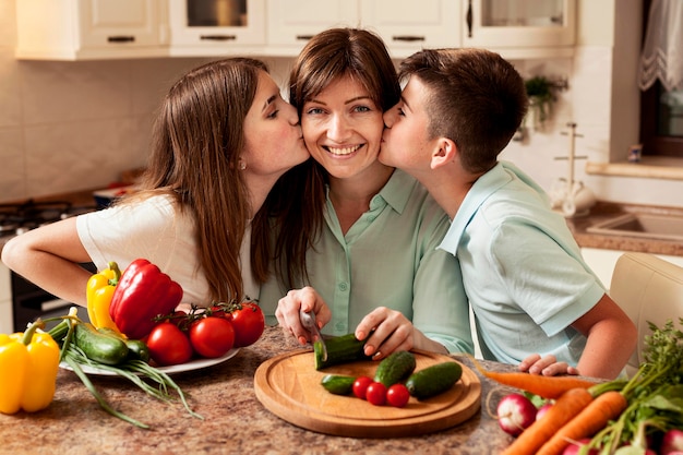 Children kissing mother in the kitchen while preparing food
