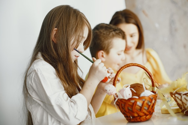 Children paint eggs. Mother teaches children. Sitting at a white table.