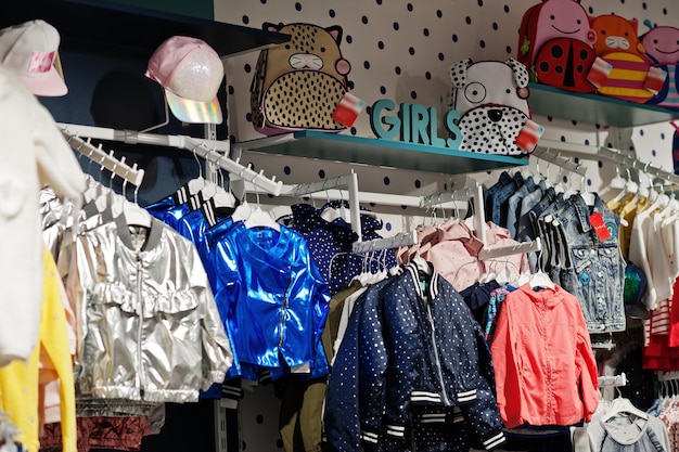 Children's bright clothes hang on the display in the baby clothing store Girls section