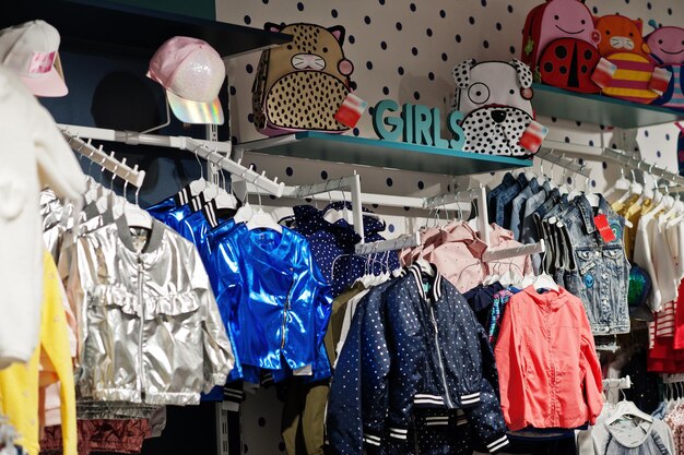 Children's bright clothes hang on the display in the baby clothing store Girls section