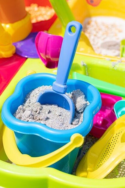 A children's bucket full of sand with a shovel stuck in the sand.
